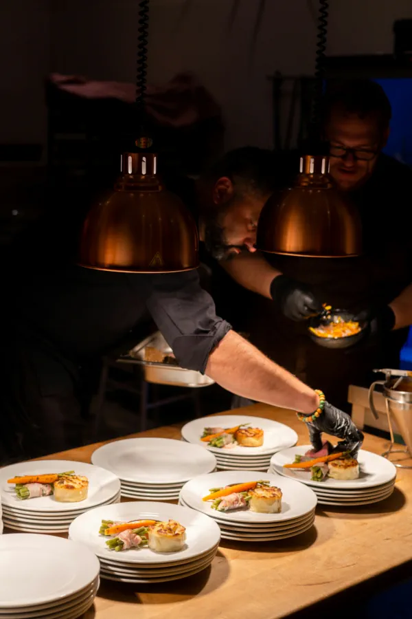 Bastidores da cozinha executiva com equipe de chefs fazendo a finalização técnica de pratos para menu degustação corporativo.