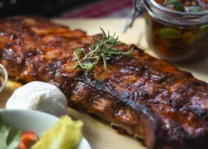 Entrecosto de porco grelhado com molho barbecue, servido numa tábua de madeira.