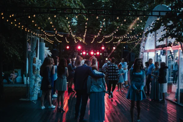 Convidados socializando em espaço para eventos in loco com estrutura externa, iluminação aconchegante e palco decorado ao fundo.